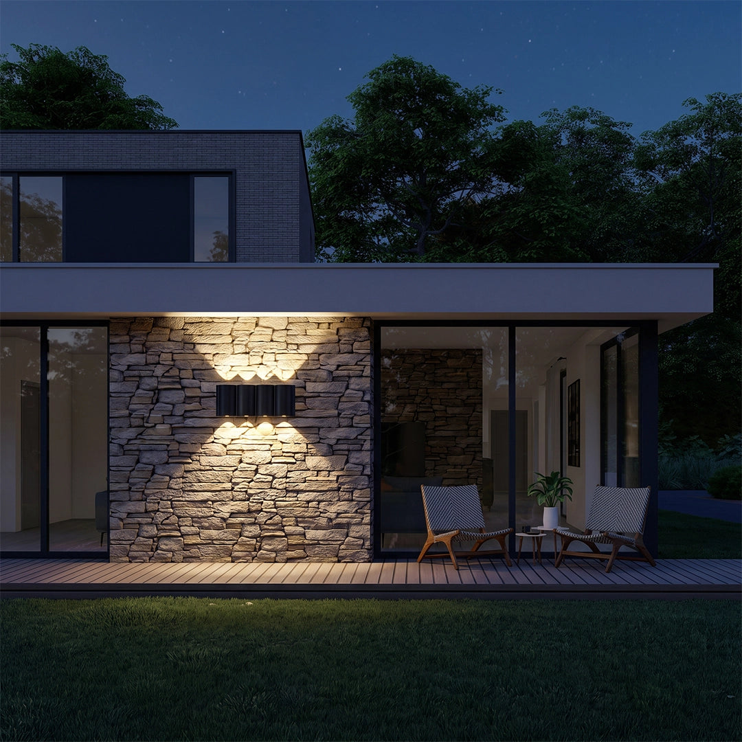 Outdoor wall light up down mounted on a stone exterior wall, casting a wide symmetrical glow across a modern patio at night.