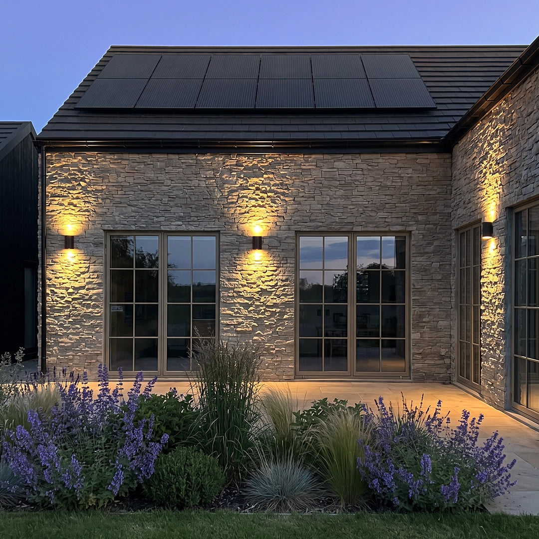 Outdoor wall light up down installed on a stone house exterior, creating warm vertical light beams along the facade at dusk.