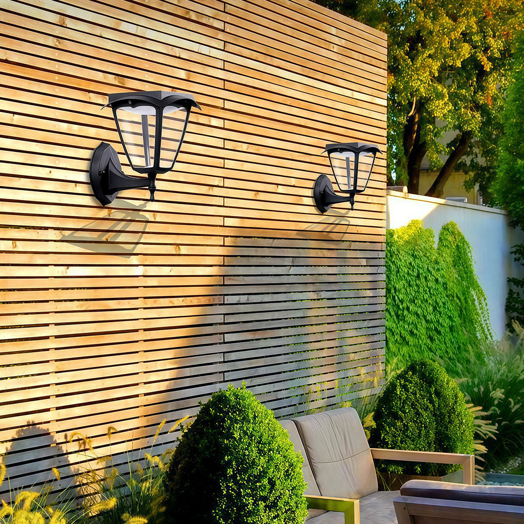 Two sets of outdoor wall lighting black lanterns casting a warm glow on a horizontal wood fence in a garden.