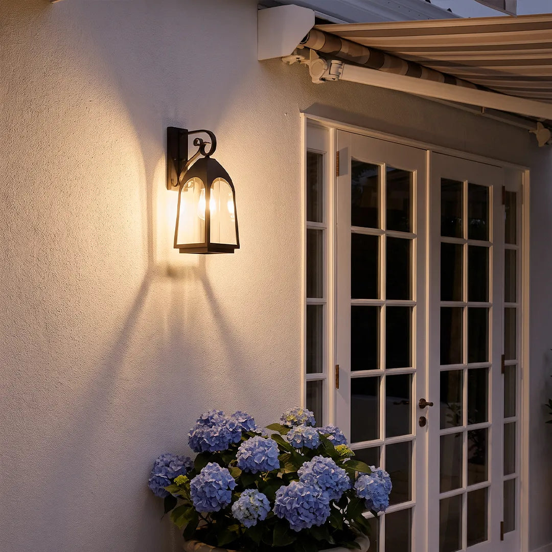 Outdoor wall mount lights glowing at dusk beside French doors and blue hydrangeas on an exterior wall.