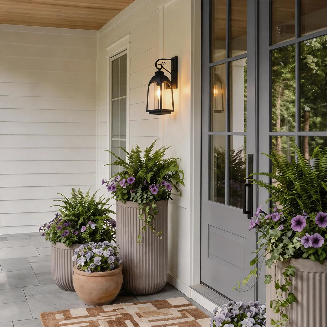 Outdoor wall mount lights beside a white entry door with large planters and purple flowers.