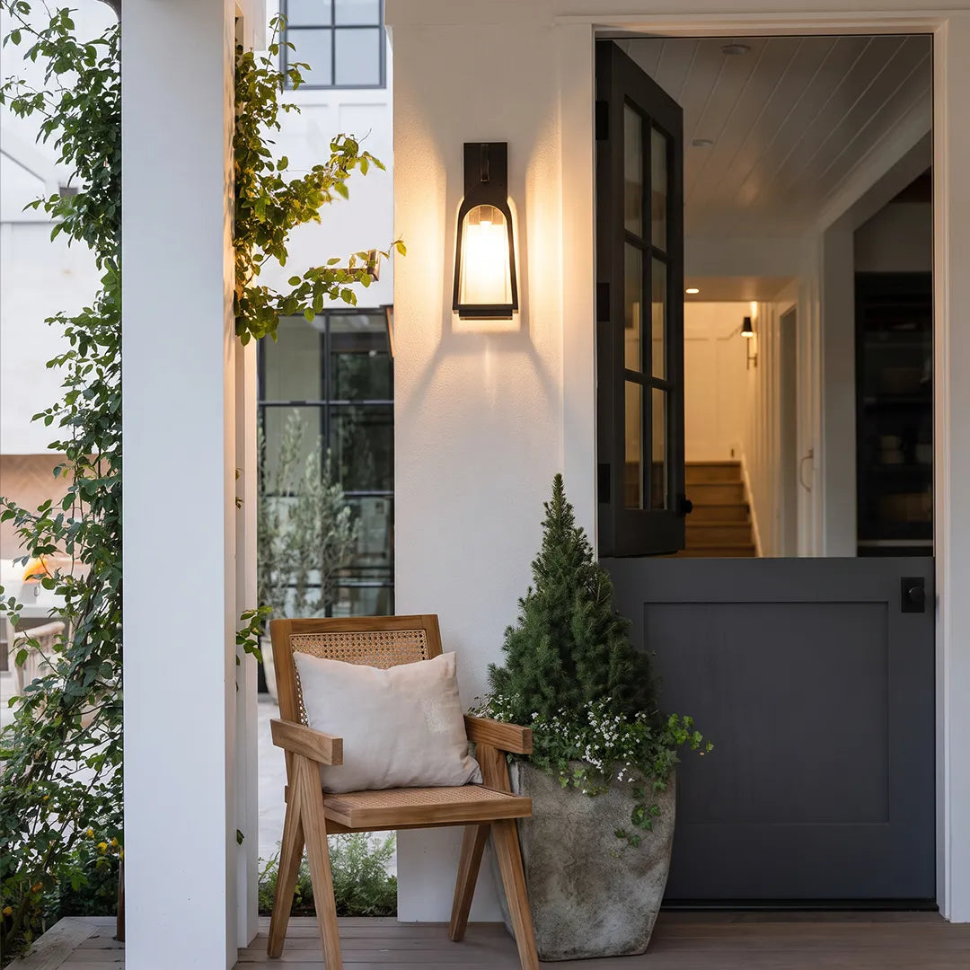 Outdoor wall mount lights installed by a modern front porch with a dark half wall and potted greenery.