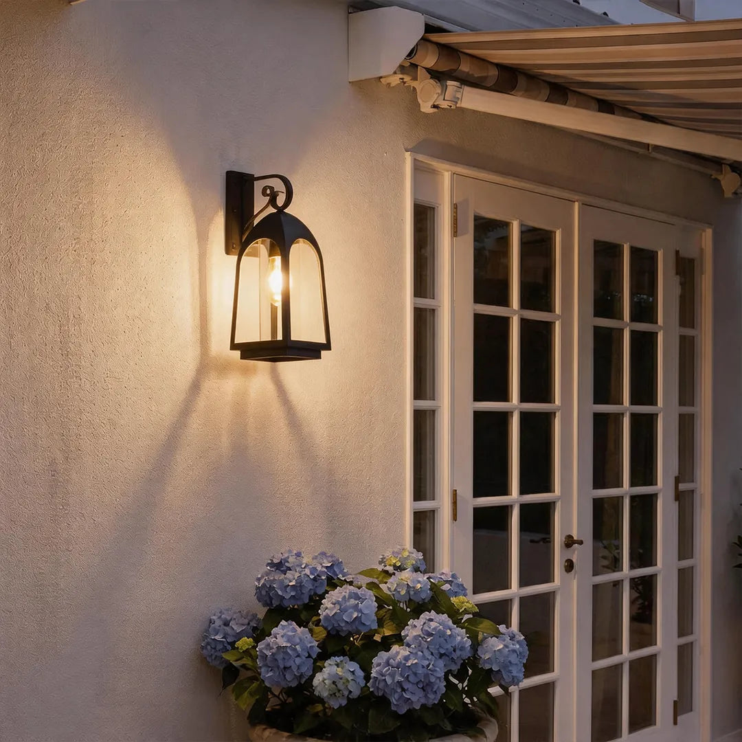 Outdoor wall mount lights glowing beside French doors on a stucco exterior at night.