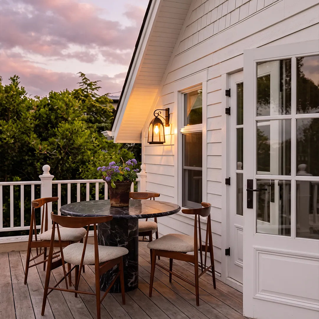 Outdoor wall mount lights illuminating a small patio dining area beside white siding and French doors.