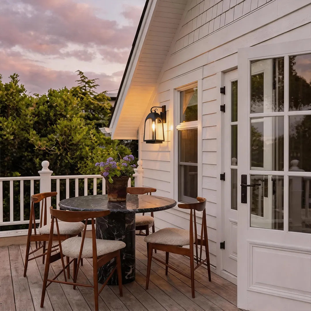 Outdoor wall mount lights beside white patio doors, illuminating a small dining area at dusk.