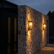 Outdoor wall mount lights installed on a textured stone exterior wall, casting warm vertical illumination beside a dark doorway.