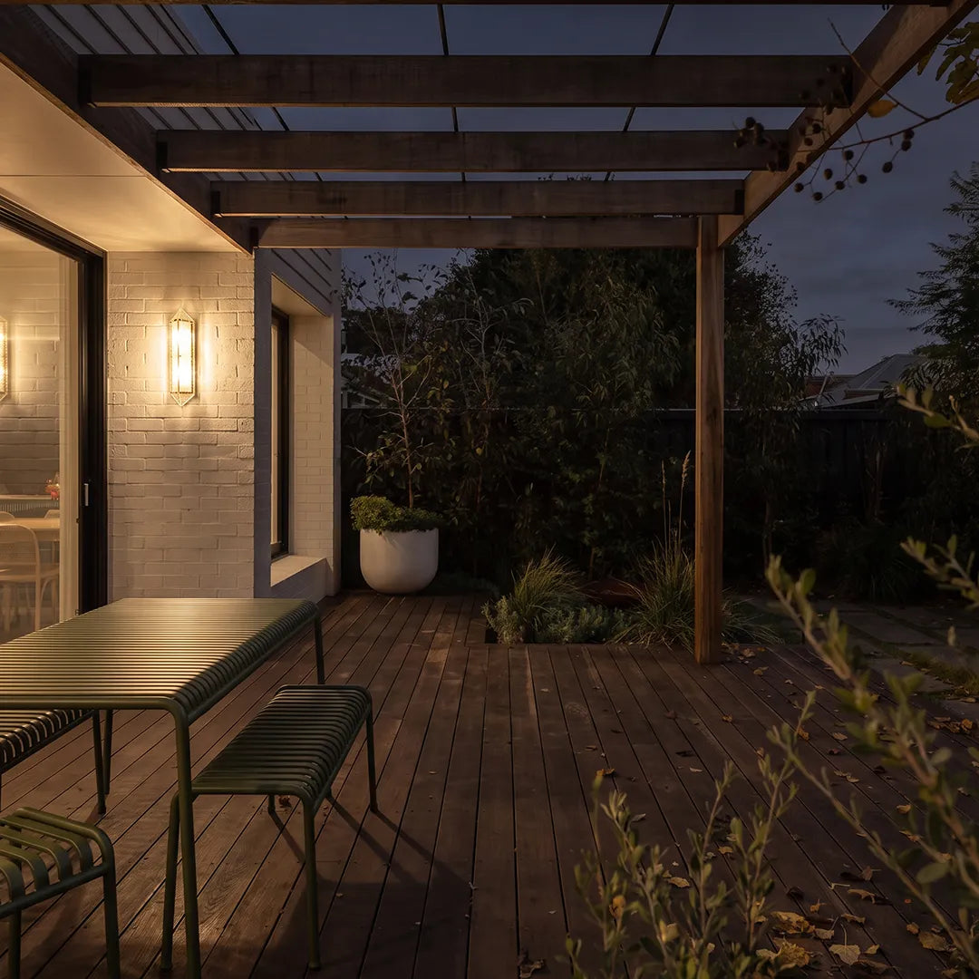 Outdoor wall sconce illuminating covered wooden deck and garden seating