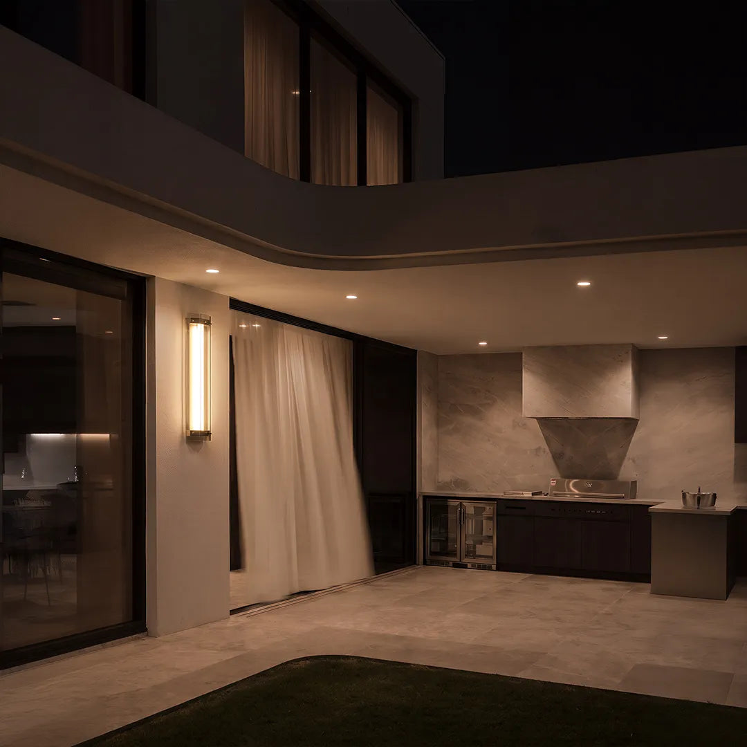 Outdoor wall sconce with warm lighting beside covered patio and outdoor kitchen