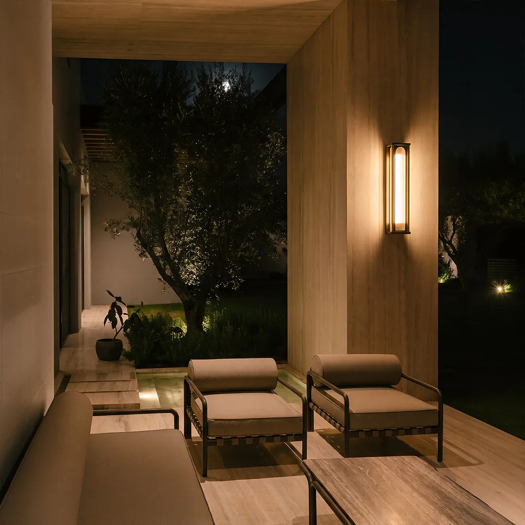 Outdoor wall sconce illuminating covered patio lounge and garden at night