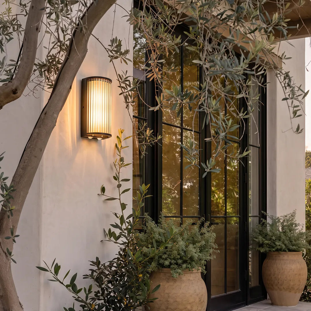 Outdoor wall sconce with ribbed glass shade beside garden patio entrance