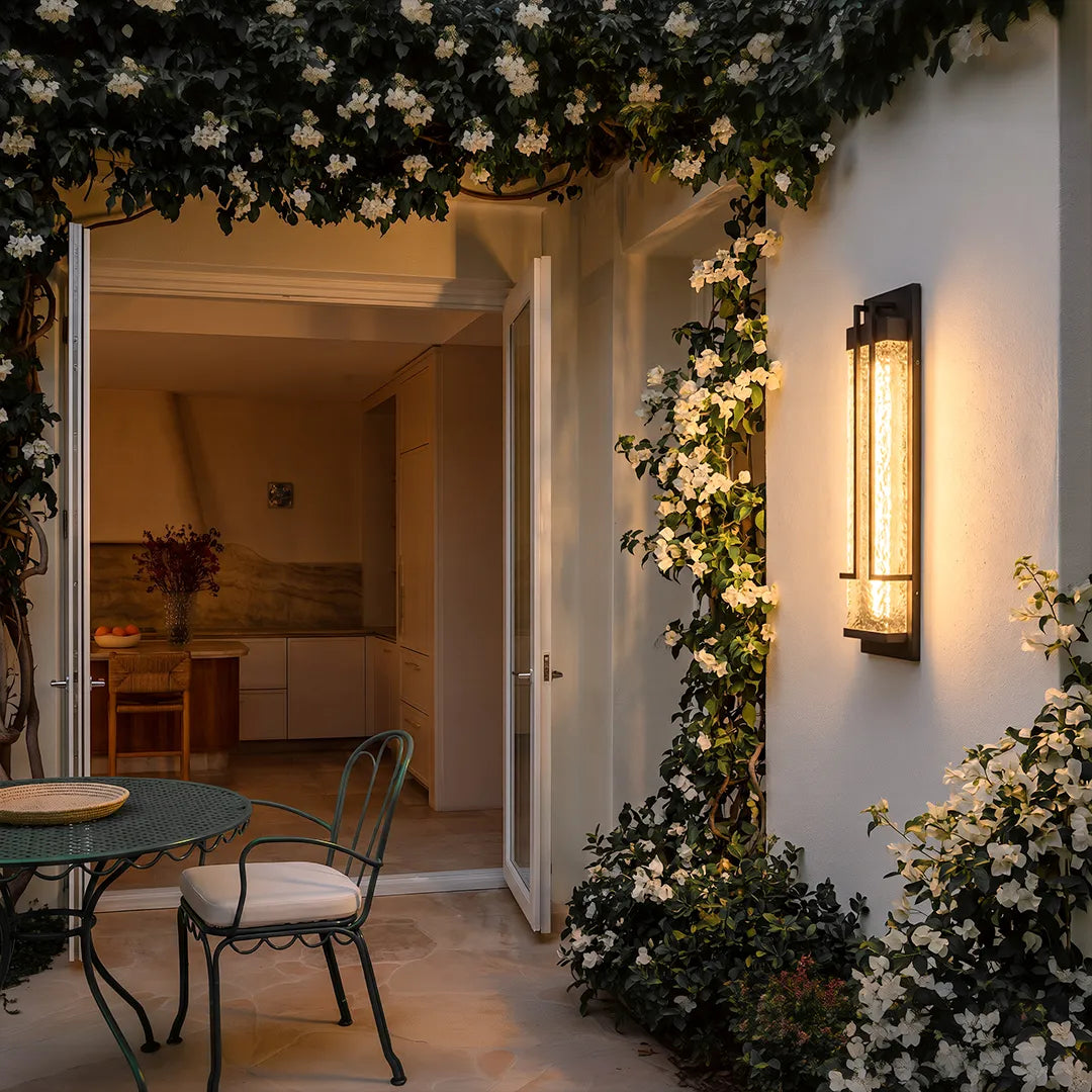 Outdoor wall sconce with warm glow beside garden patio and climbing flowers
