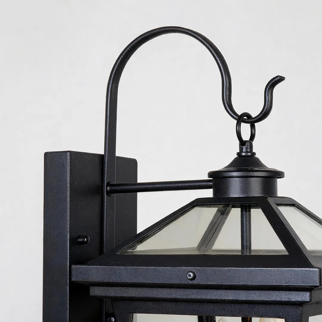 Outdoor wall sconce light close-up showing the curved gooseneck arm, black backplate, and lantern top frame.
