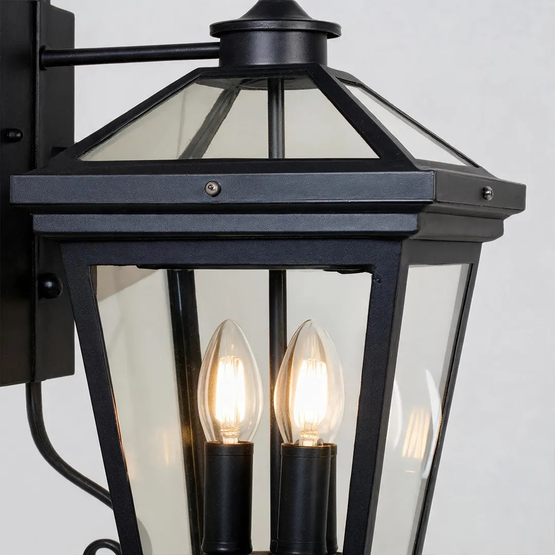 Outdoor wall sconce light detail showing the black lantern frame, clear glass panels, and candle-style bulbs.