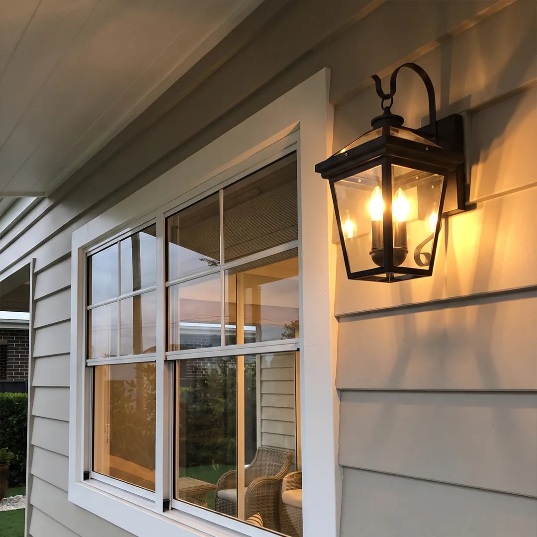 Outdoor wall sconce light mounted beside a porch window, casting warm illumination across horizontal exterior siding.