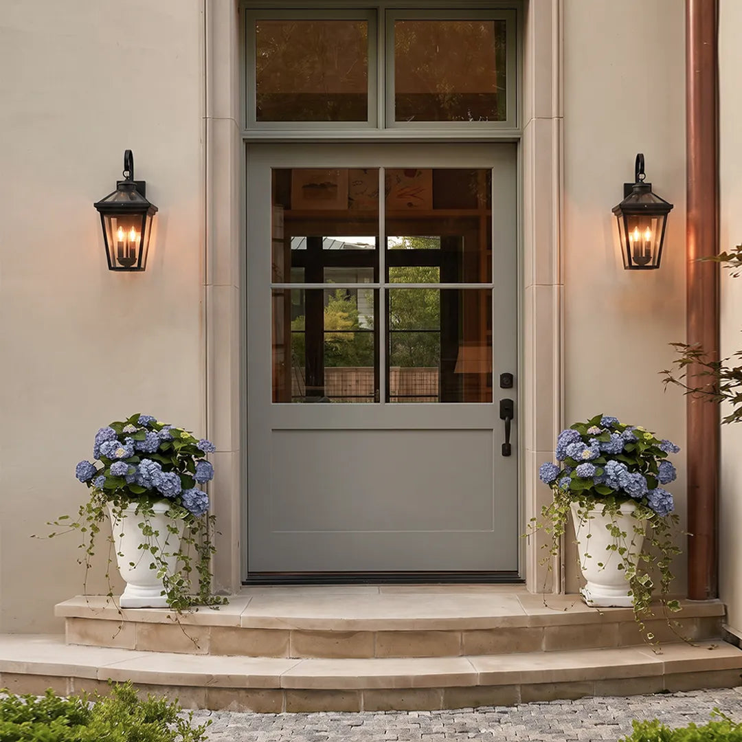 Outdoor wall sconce lights flanking a front entry door with planters, creating a balanced and welcoming exterior lighting design
