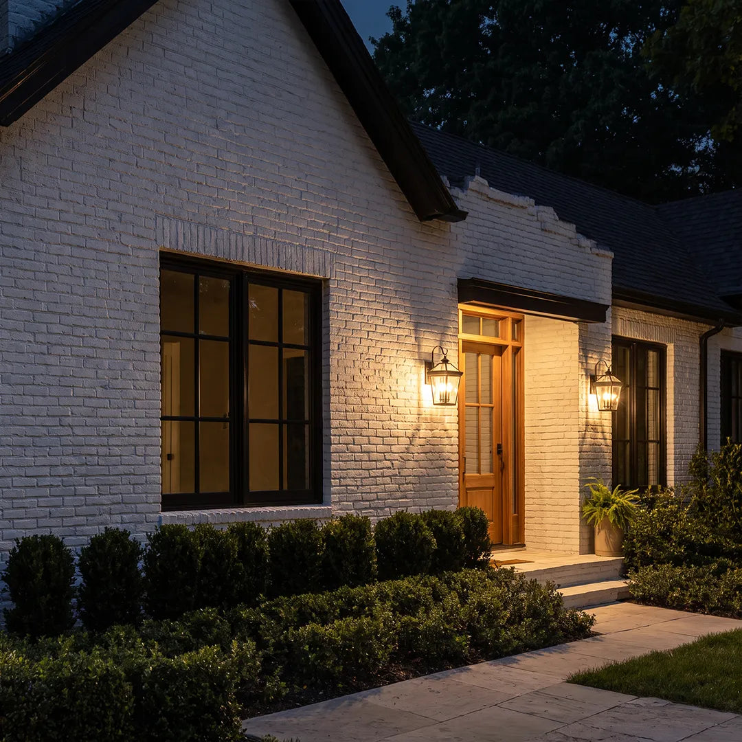 Outdoor wall sconce lights installed on a white brick house exterior, highlighting the front door and walkway at night.
