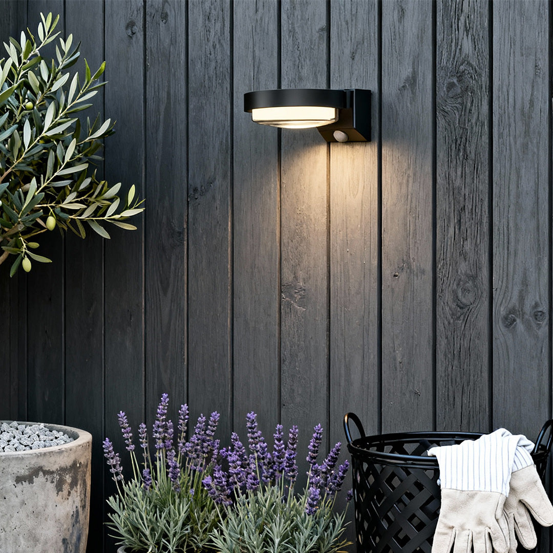 Modern black outdoor wall sconce installed on wood siding with warm inviting light.