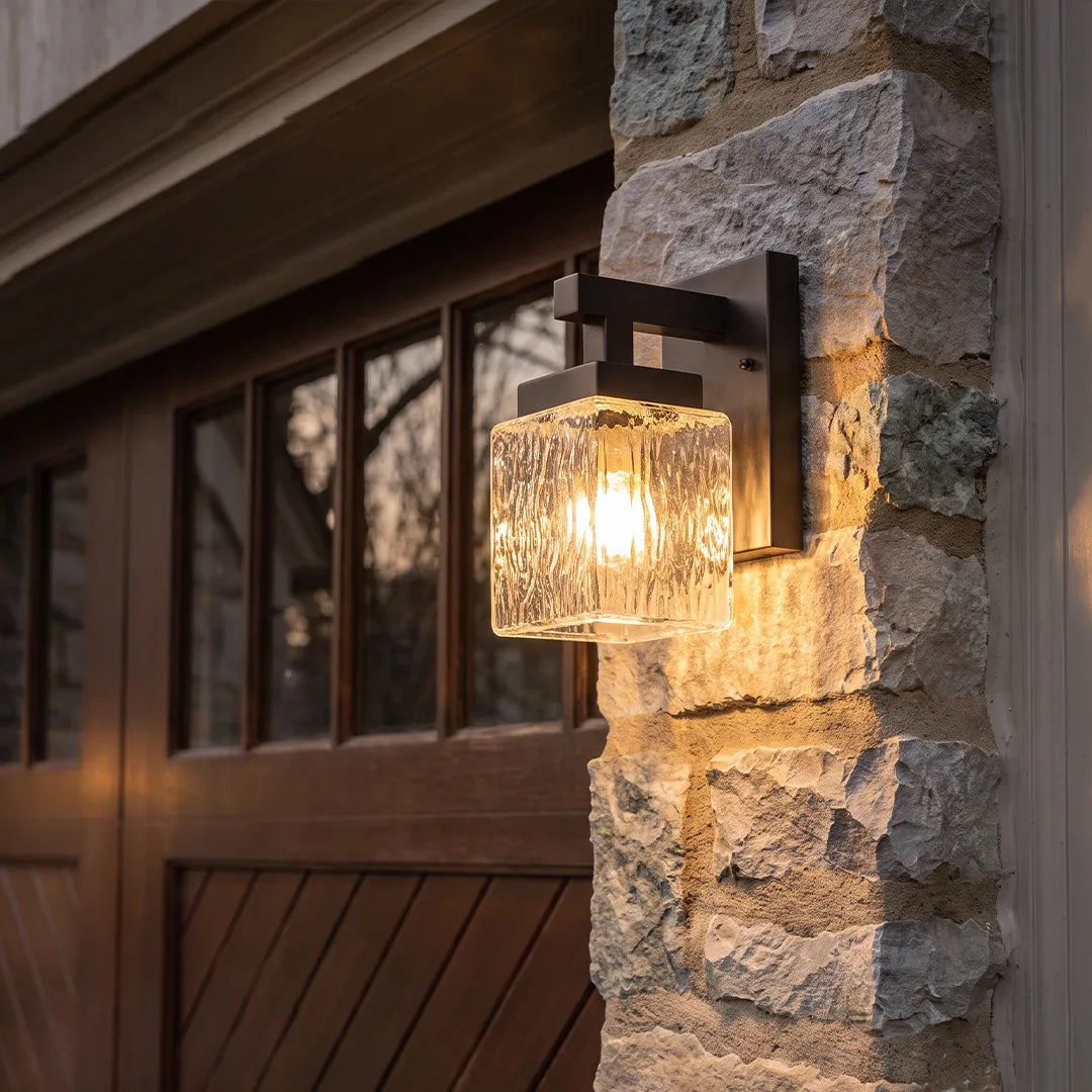 Outdoor wall sconce with textured glass shade beside stone garage exterior