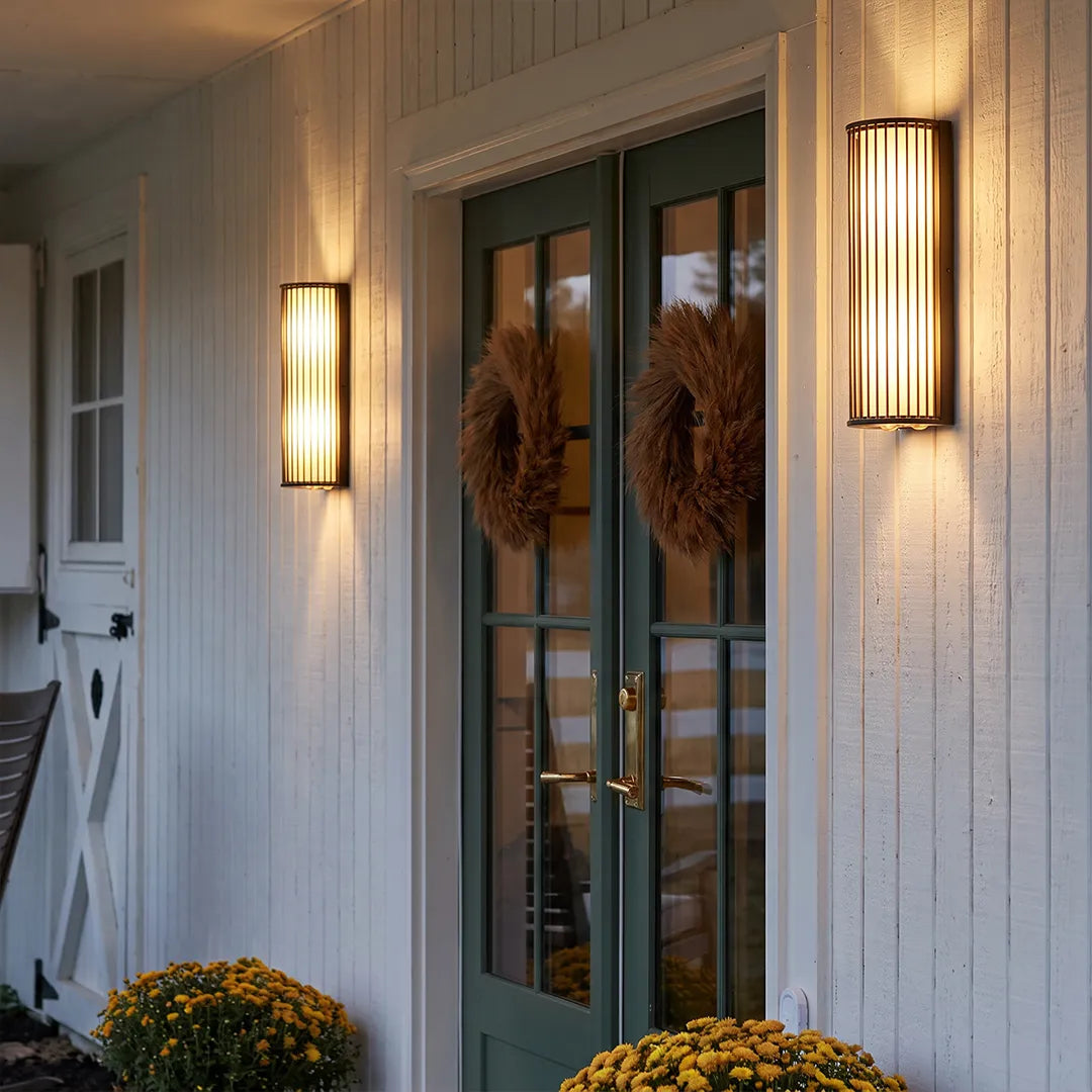 Outdoor wall sconces with warm glow beside covered porch and glass doors