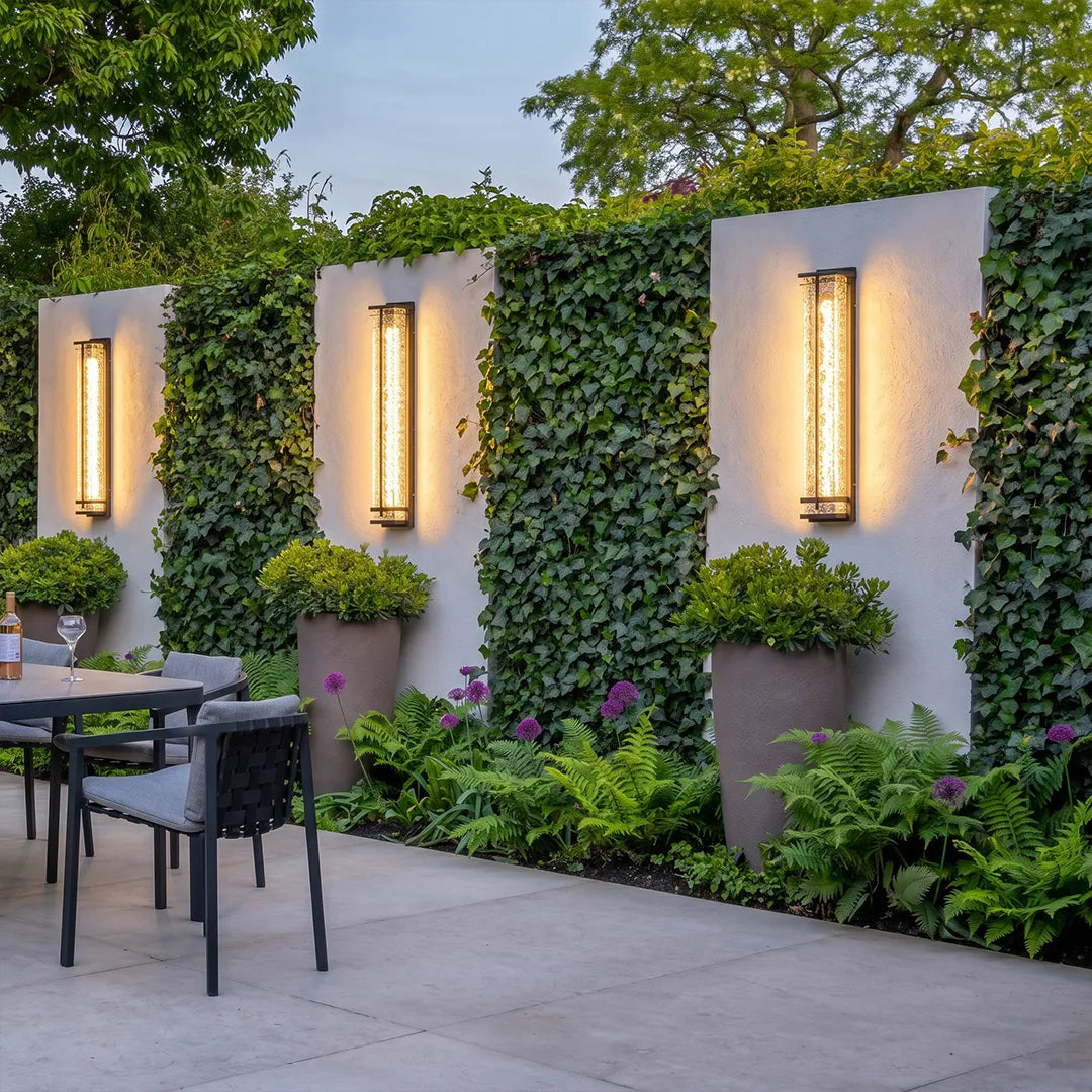 Outdoor wall sconces with warm glow on garden privacy wall with climbing plants