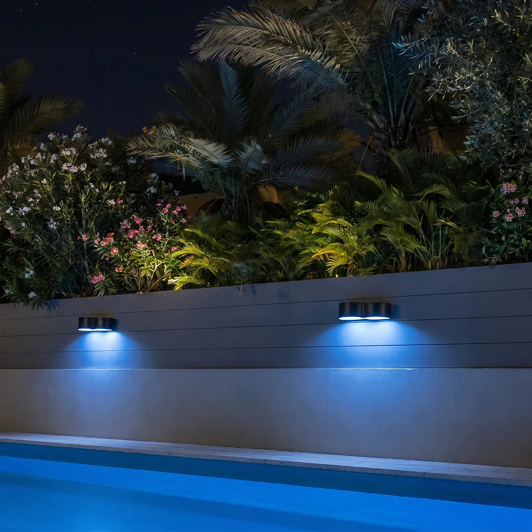 Outdoor wall wash lighting casting blue accent light along a poolside wall and tropical landscape.