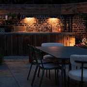 Outdoor wall wash lighting illuminating a brick patio dining area and outdoor kitchen wall at night.