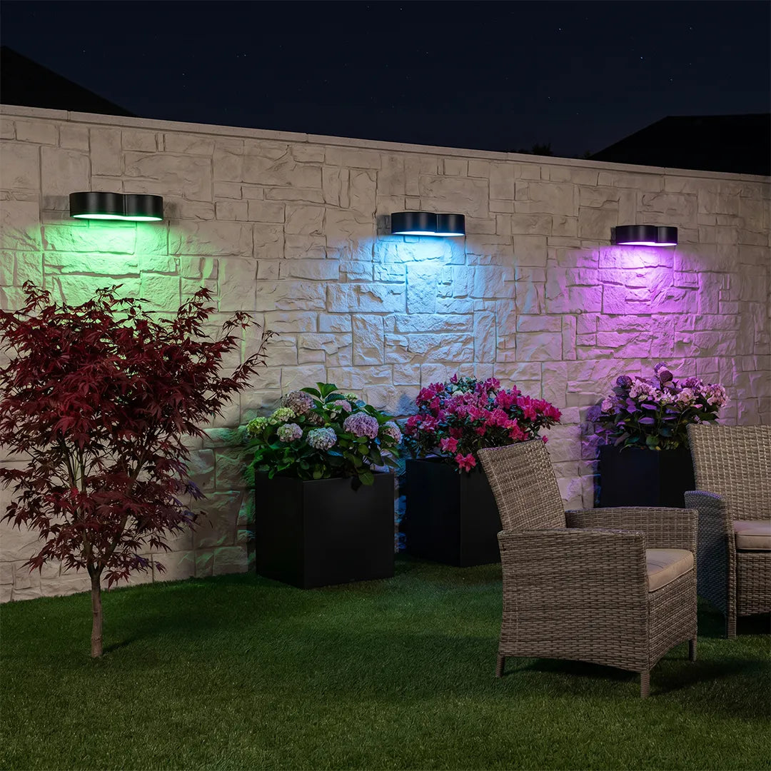Outdoor wall wash lighting in color-changing green, blue, and purple tones decorating a backyard wall.