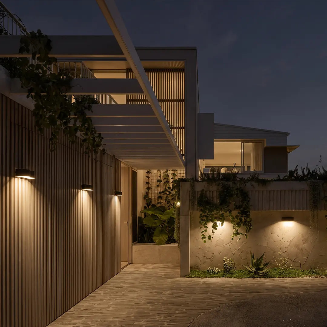 Outdoor wall wash lighting installed along a modern covered walkway and garden fence at dusk.