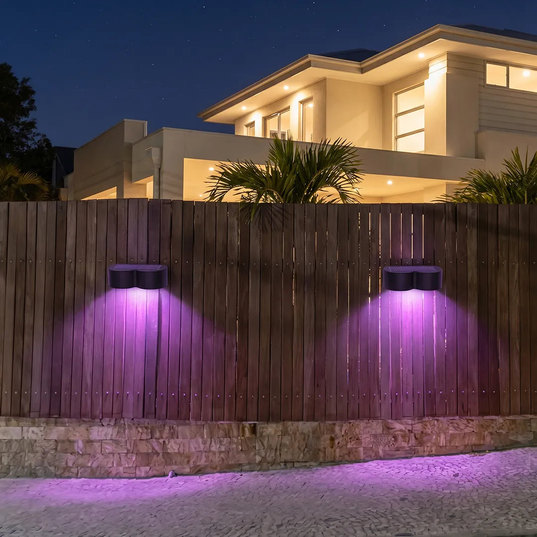 Outdoor wall wash lighting projecting purple accent beams onto a backyard fence in front of a modern house.