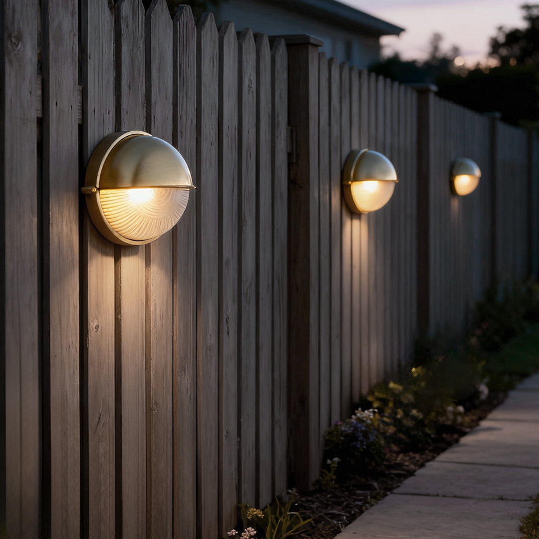 Row of oval bulkhead outdoor lights mounted on a wooden fence, providing pathway illumination at dusk.