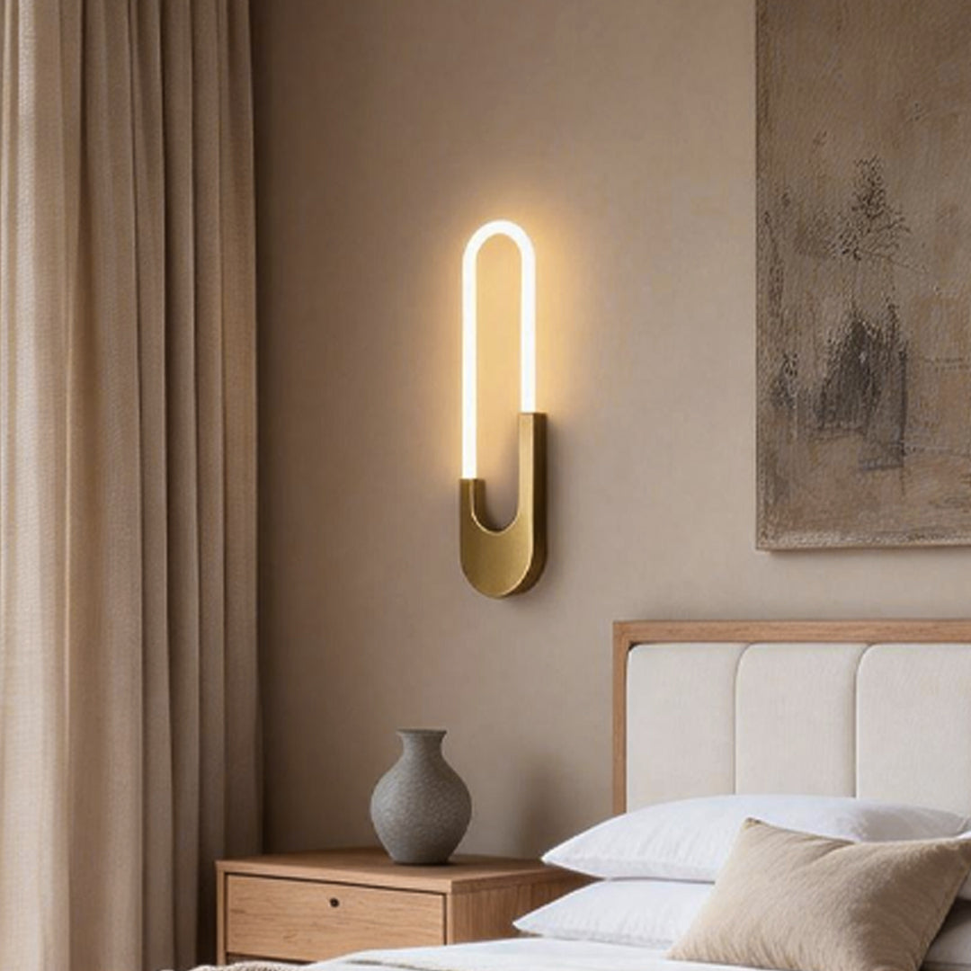 A modern oval LED wall sconce with sleek black and gold design, providing ambient lighting to a cozy bedroom.