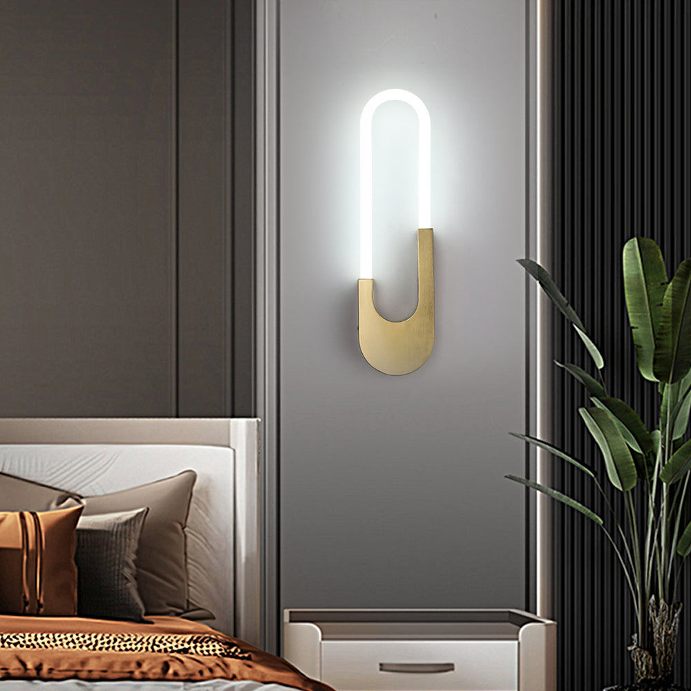 A stylish oval LED wall sconce in black and gold, mounted above a bed for ambient lighting in a modern bedroom.