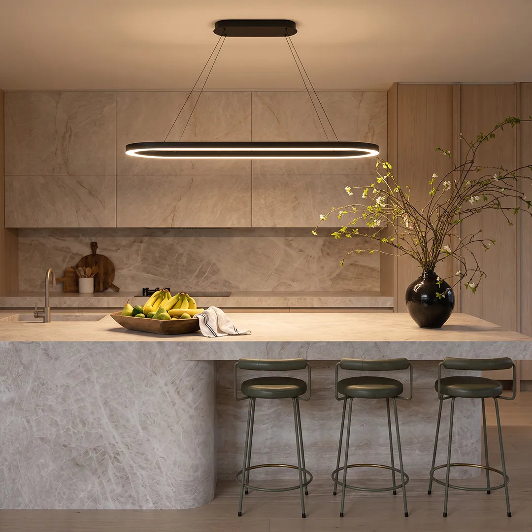 Oval pendant light hanging above a marble kitchen island with bar stools in a modern open kitchen.