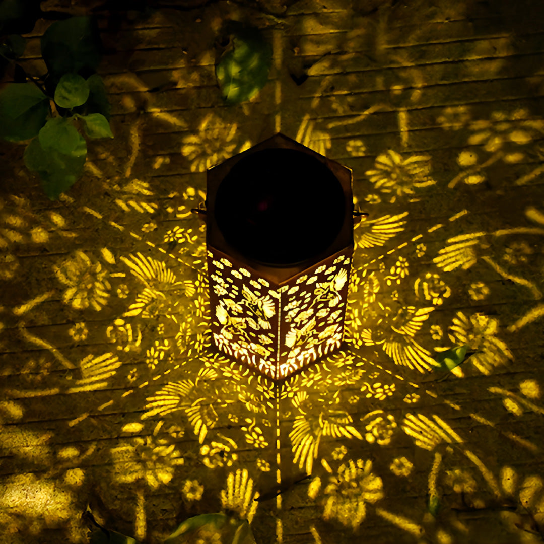Overhead view of a lit red outdoor lantern projecting dense floral patterns onto ground surfaces at night.