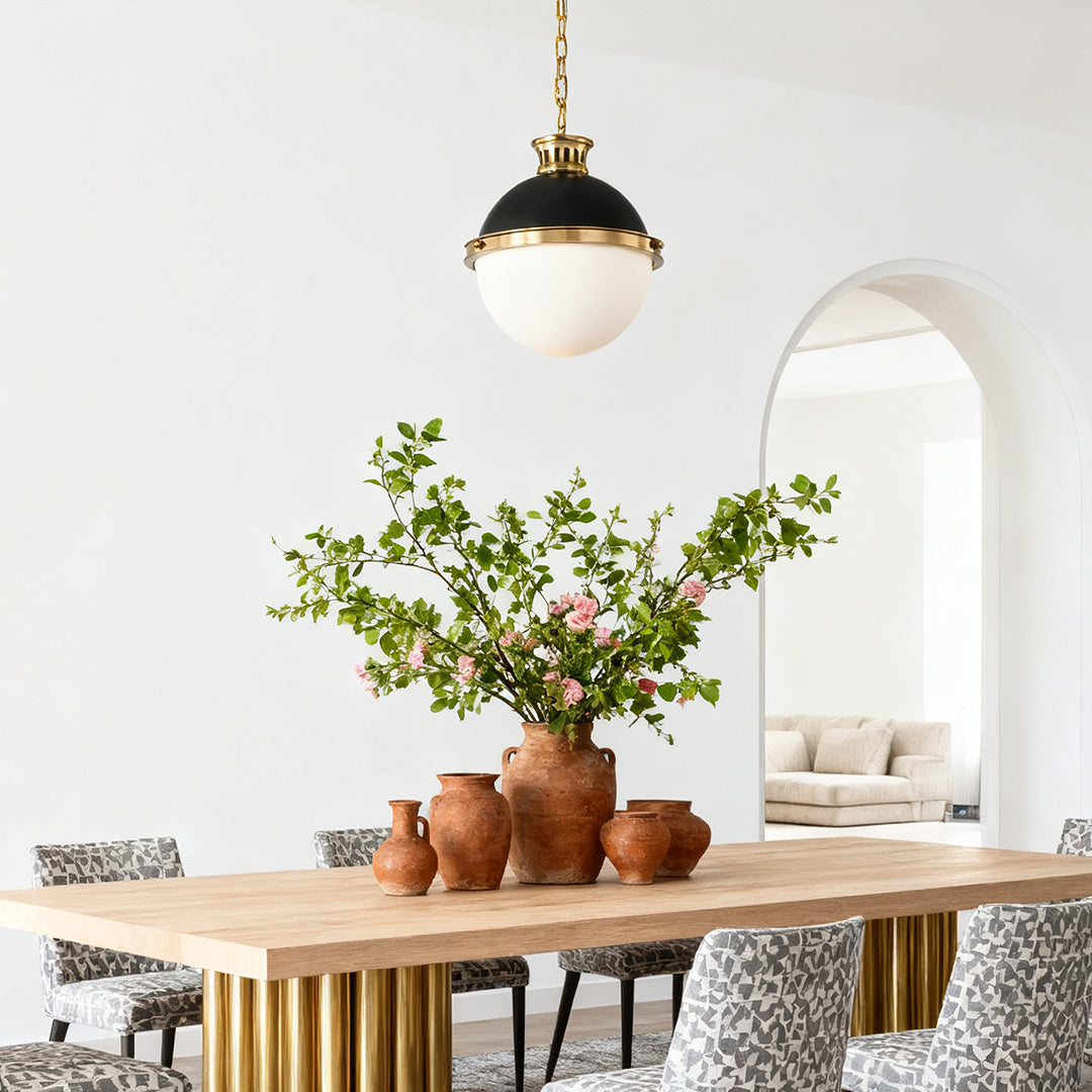 Oversized ball pendant light providing ambient light above a natural wood dining table in a room with a decorative arched doorway.