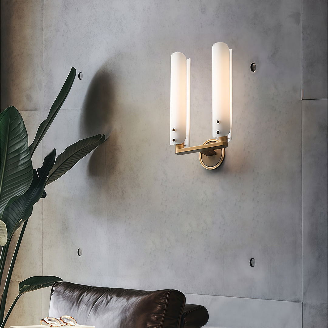 Pair of brass wall lights with glass shades illuminating bedroom with plant and artwork accents.