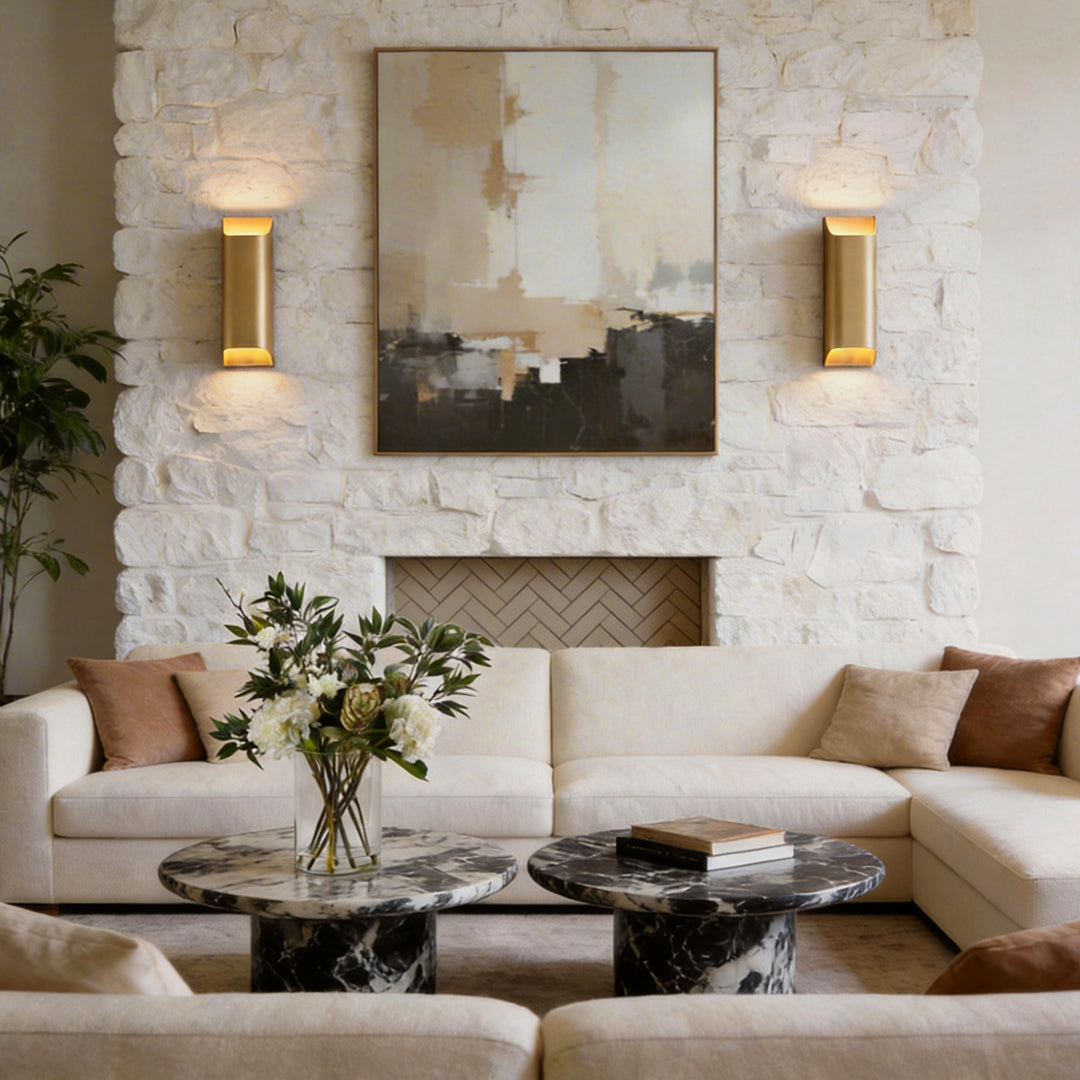 Pair of brass wall lights illuminating a white stone fireplace and artwork in a modern lounge.