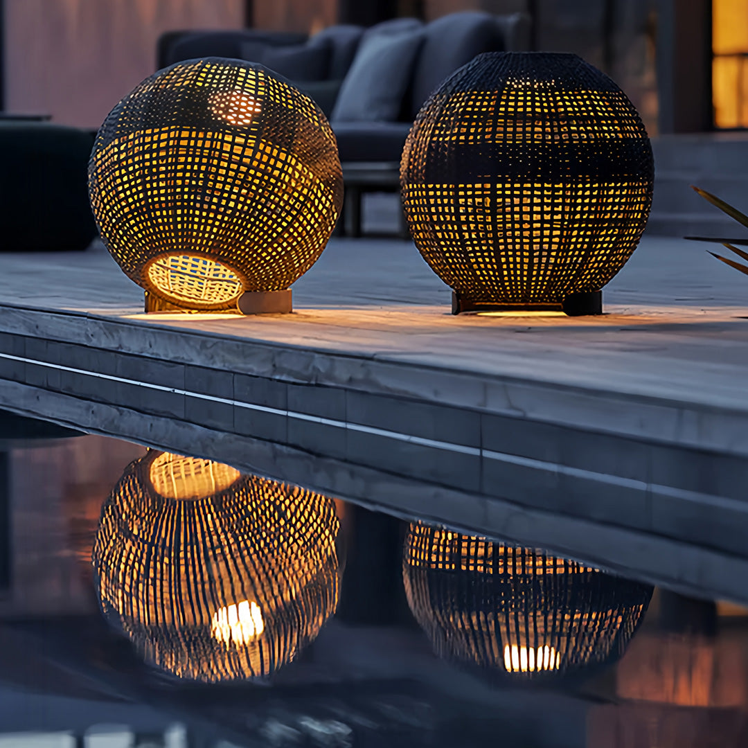 Pair of dark gray woven outdoor globe lantern lights reflecting on a poolside wooden deck in the evening.