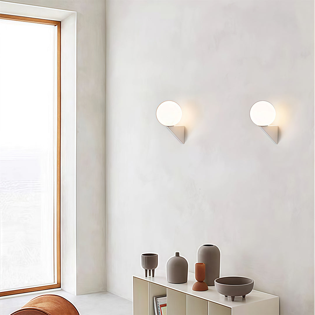 Pair of white frosted globe wall lights illuminating a collection of terracotta vases on a shelf in a warm, textured room.