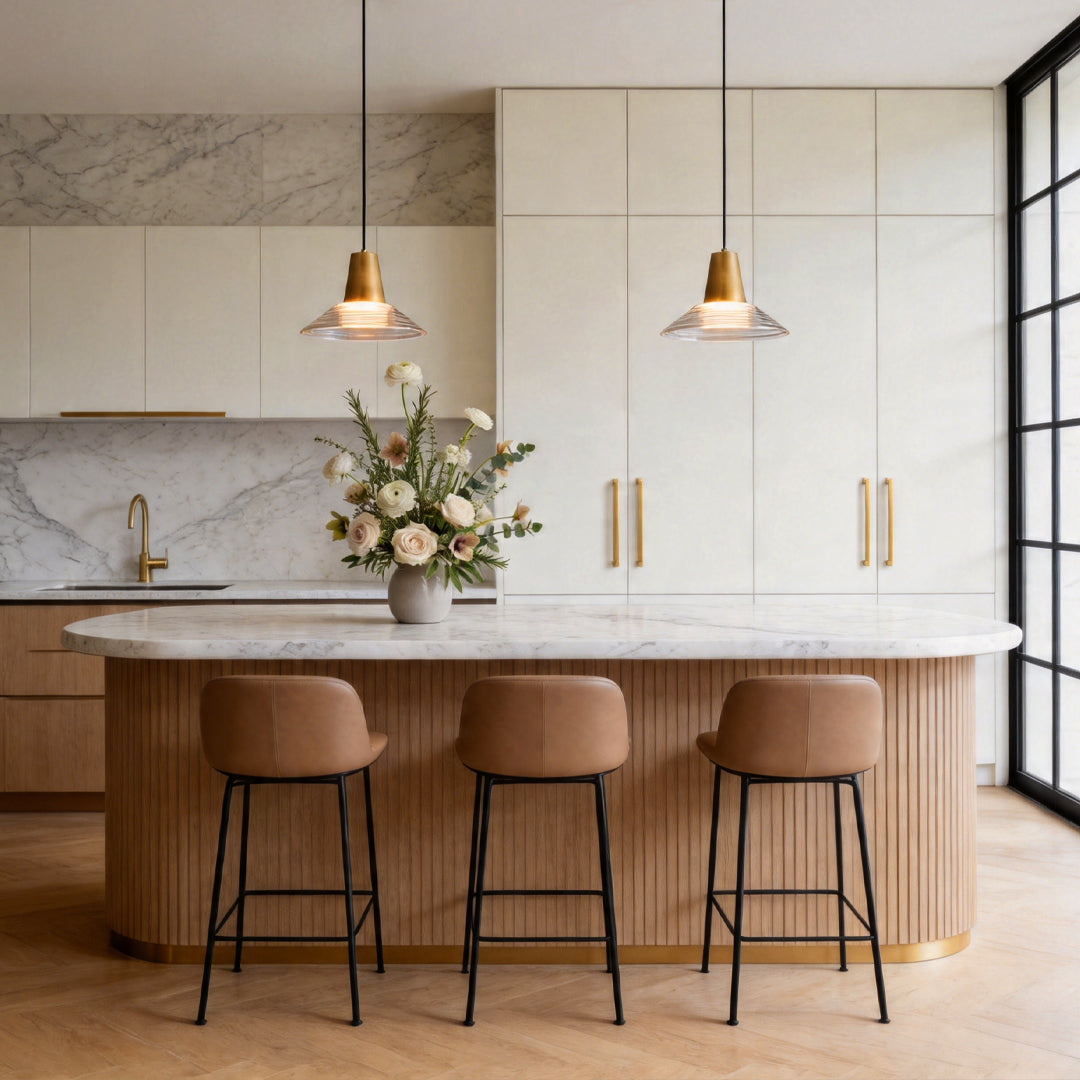 Pair of glass cone pendant light fixtures hanging above a marble kitchen island with stools ok.