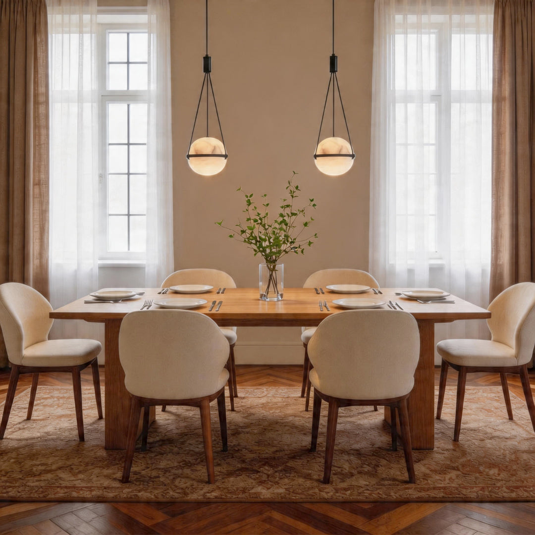 Pair of globe pendant light fixtures hanging above a wood dining table with six creamy chairs.