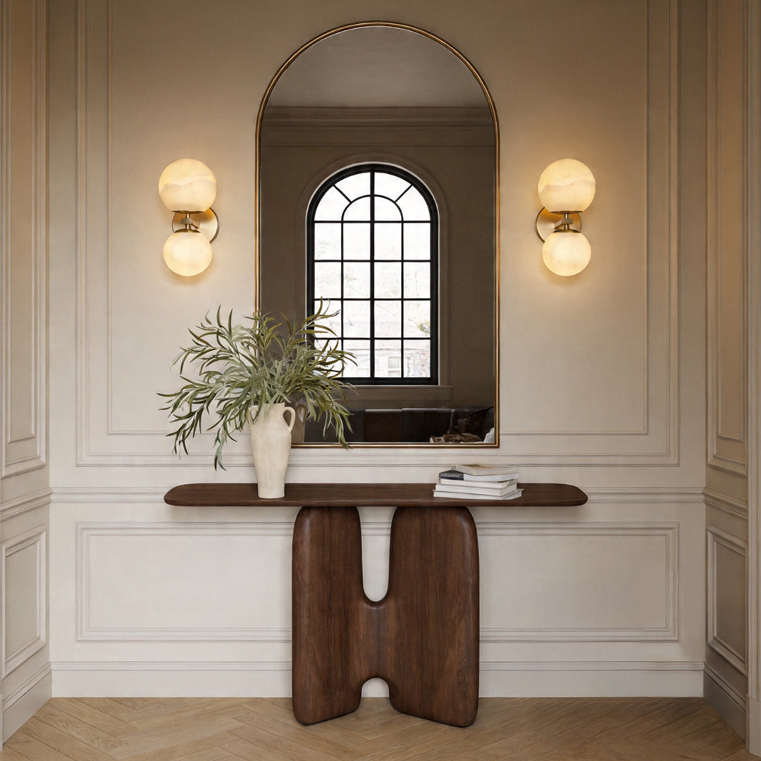 Pair of globe wall lights flanking a tall arched mirror above a unique dark wood console table.