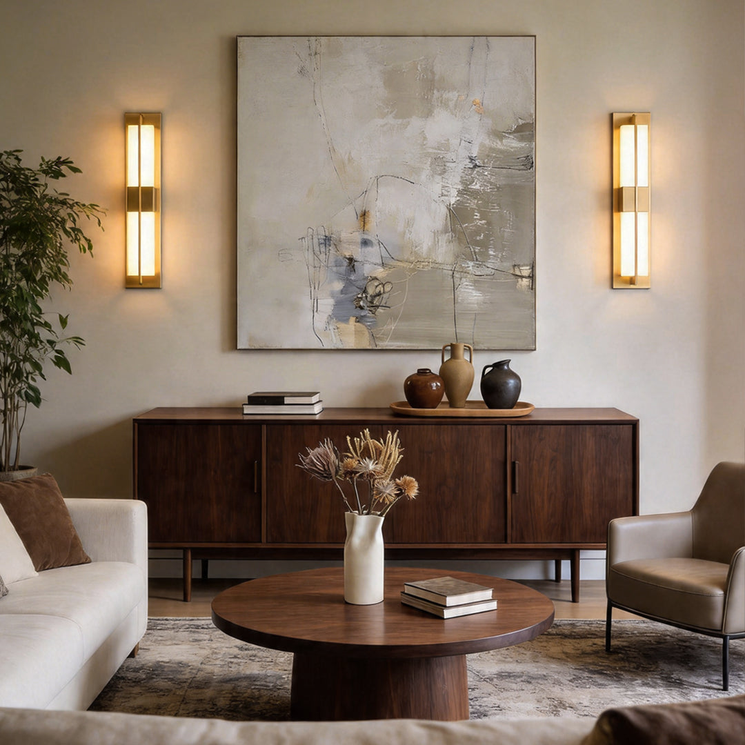 Pair of gold wall lighting fixtures flanking abstract art above a dark wood sideboard table.