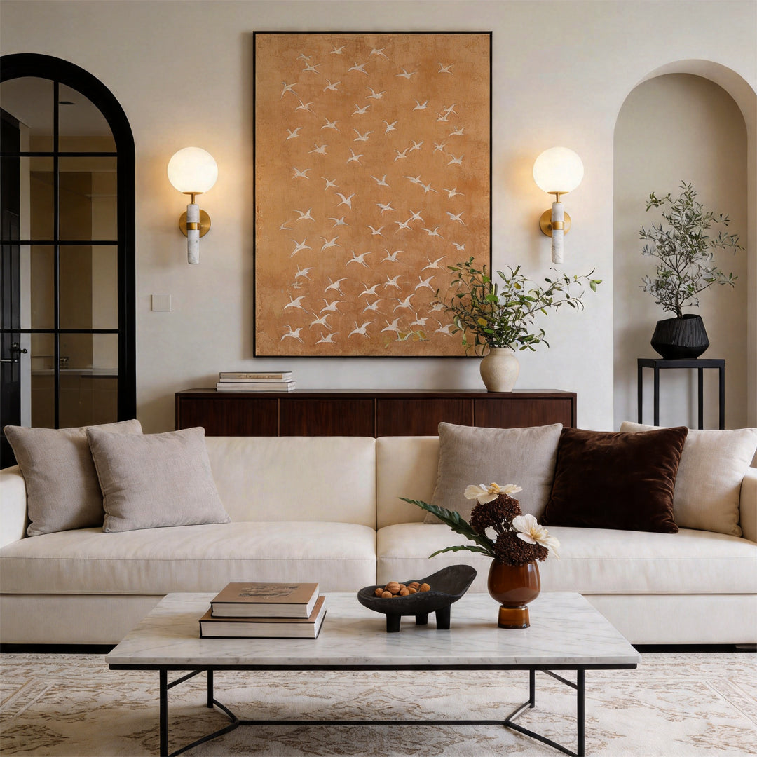 Pair of gold wall sconce lighting fixtures flanking abstract art above a white fabric sofa.