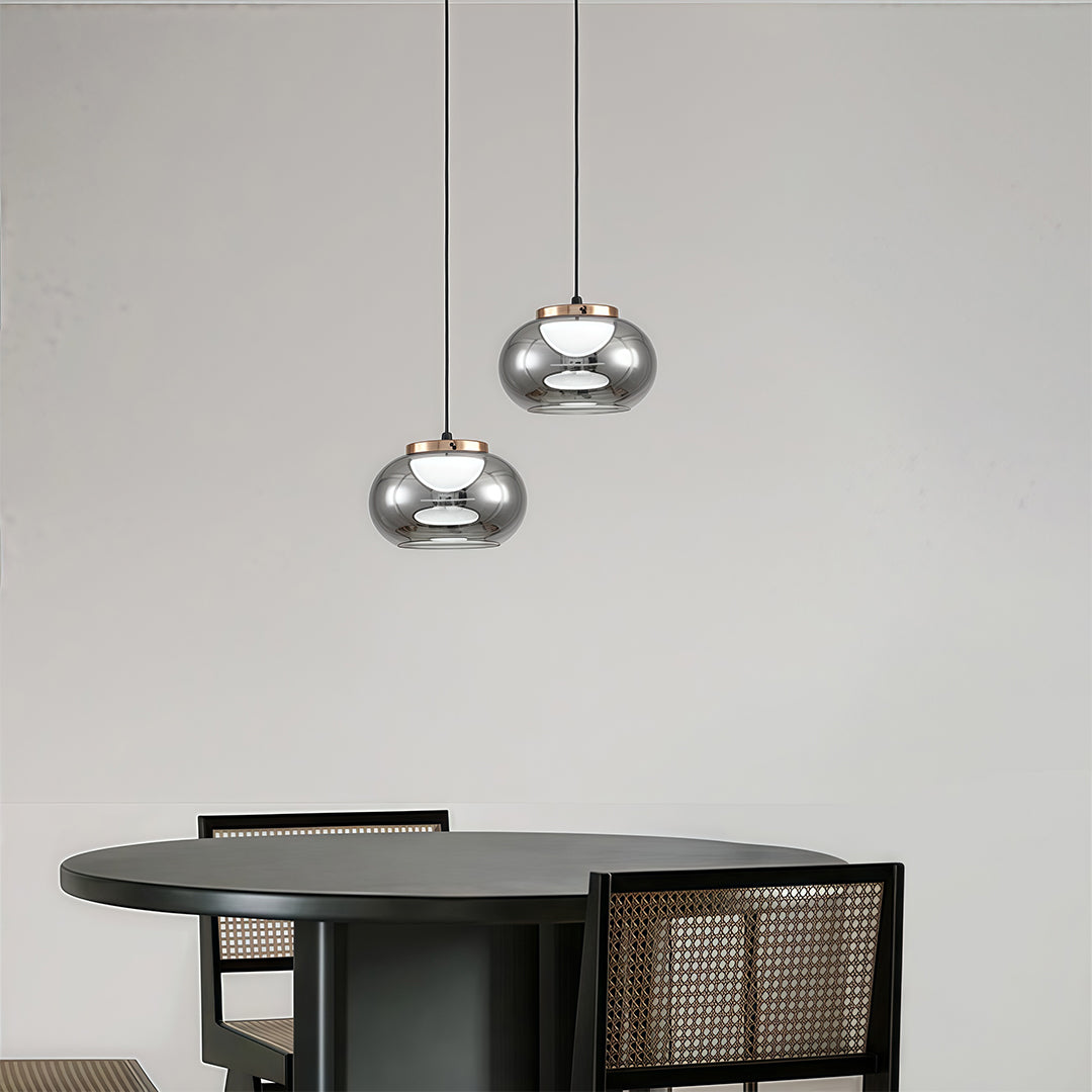 Pair of gray glass pendant lights with gradient smoke finish hanging above modern black kitchen island.