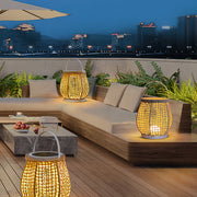Pair of illuminated woven outdoor lanterns with white bases, creating a cozy ambiance on a modern rooftop patio lounge at night.