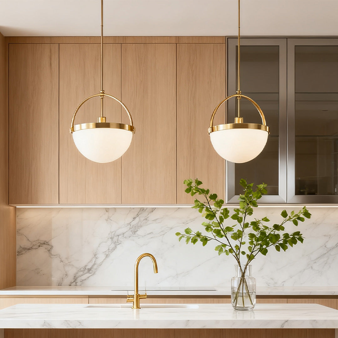 Pair of gold and white pendant light fixtures illuminating a light wood kitchen with marble backsplash and a golden-colored faucet.