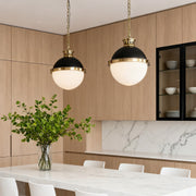 Pair of modern ball pendant light fixtures with black and brass hardware hanging over a sleek, light wood kitchen island.