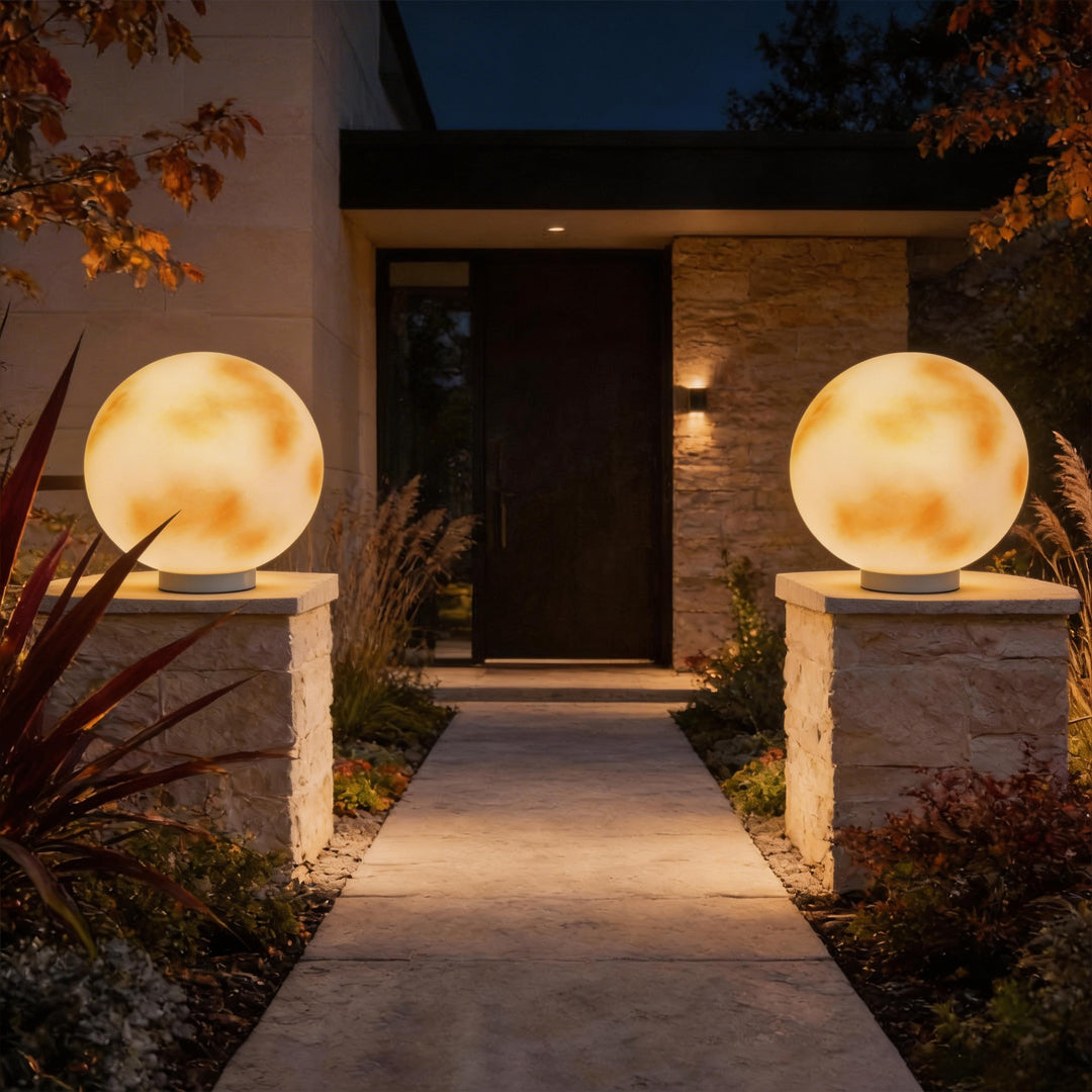 Pair of moon-shaped stone pillar lights flanking a modern home entrance walkway at night time.