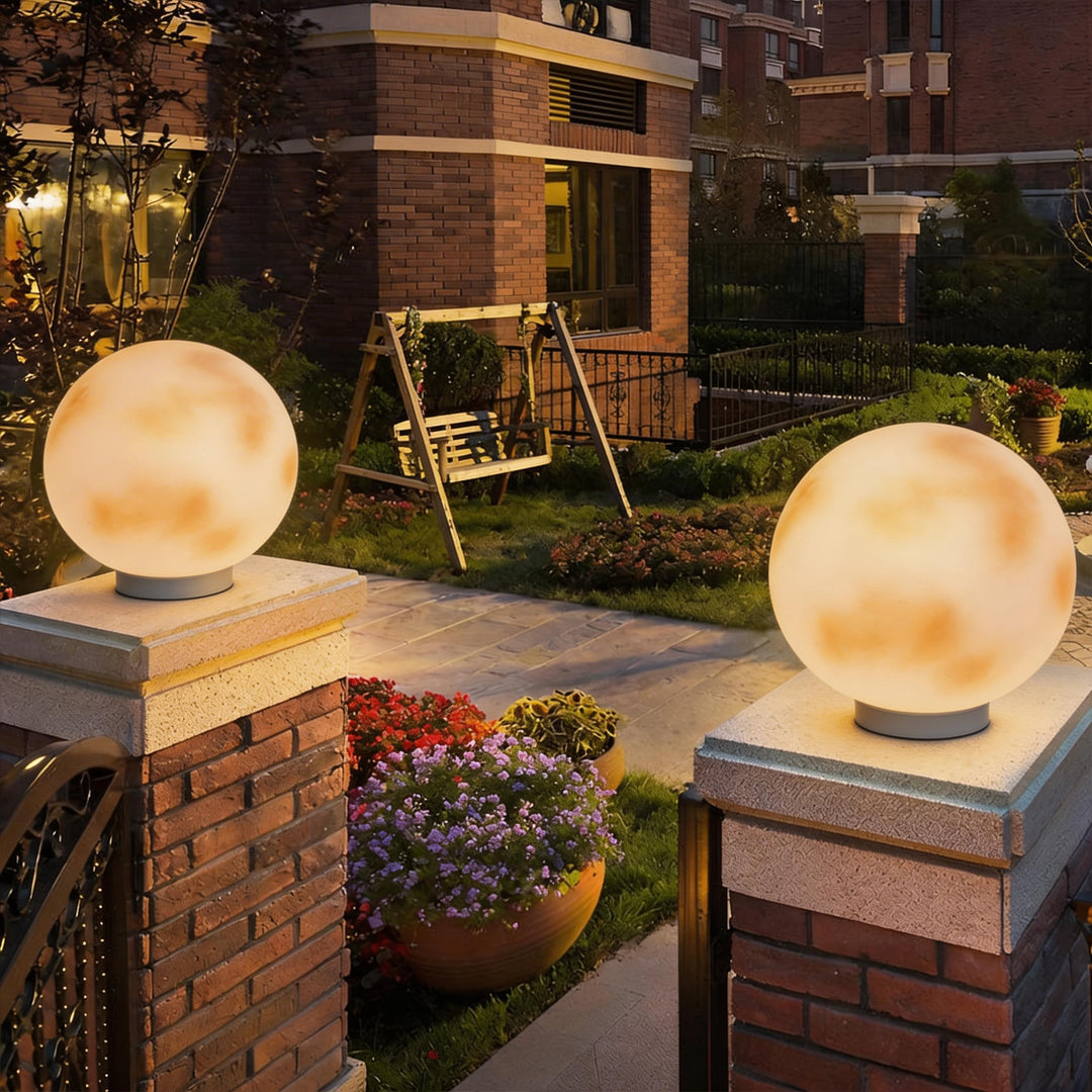 Pair of moon-shaped stone pillar lights on red brick pillars in a garden with colorful flowers.